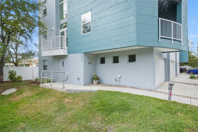 back of property with a balcony, an attached garage, fence, and a lawn