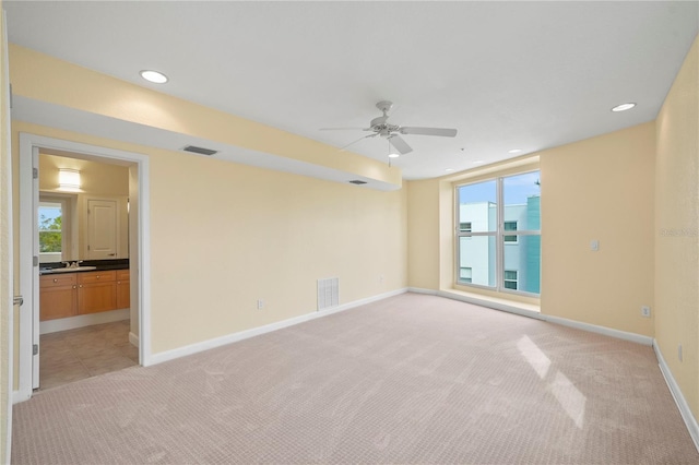 empty room with visible vents, light colored carpet, a healthy amount of sunlight, and a ceiling fan