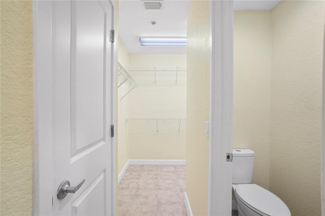 bathroom with visible vents, toilet, baseboards, a spacious closet, and a textured wall