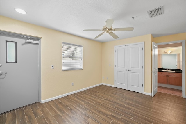 unfurnished bedroom with visible vents, dark wood-type flooring, baseboards, a closet, and a sink