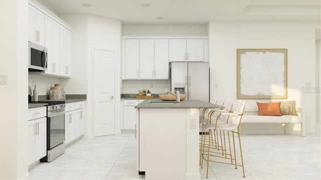 kitchen with dark countertops, a breakfast bar, stainless steel appliances, white cabinetry, and a kitchen island with sink