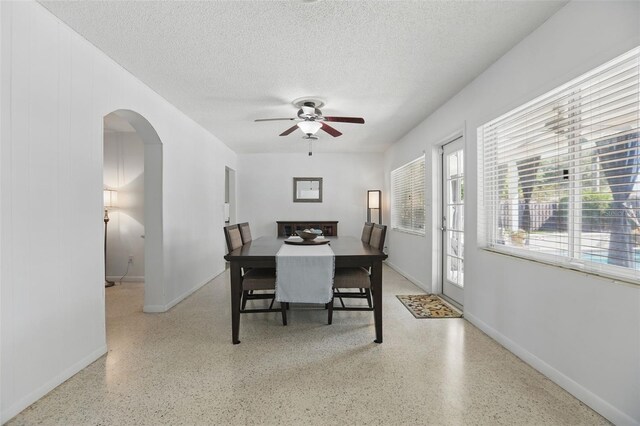 1005 Catalpa Ln, Orlando, FL 32806 - dining space with arched walkways, a textured ceiling, speckled floor, a ceiling fan, and baseboards
