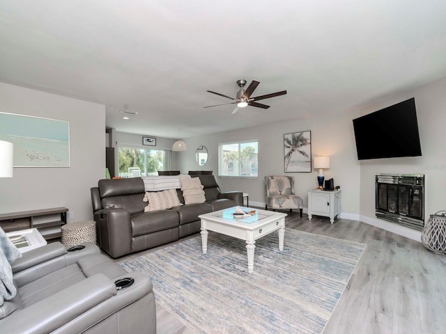 living room with a ceiling fan, a glass covered fireplace, wood finished floors, and baseboards