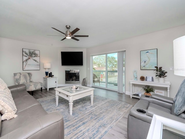 living room featuring a glass covered fireplace, wood finished floors, baseboards, and ceiling fan