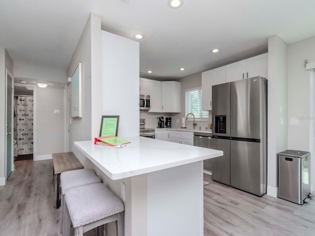 kitchen featuring a breakfast bar area, light wood-style flooring, recessed lighting, white cabinets, and stainless steel appliances