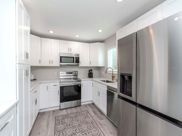 kitchen featuring white cabinets, appliances with stainless steel finishes, light wood-style floors, and a sink