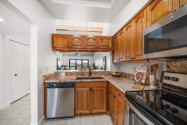 kitchen featuring brown cabinets, light stone countertops, stainless steel appliances, and a sink