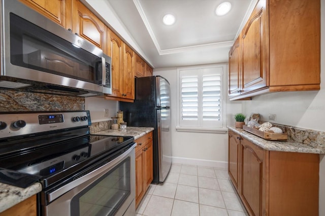 kitchen with light stone counters, brown cabinetry, baseboards, light tile patterned floors, and stainless steel appliances