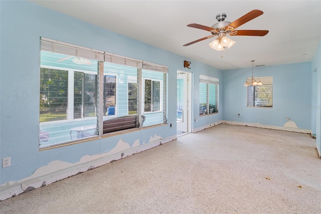 empty room with ceiling fan with notable chandelier and speckled floor