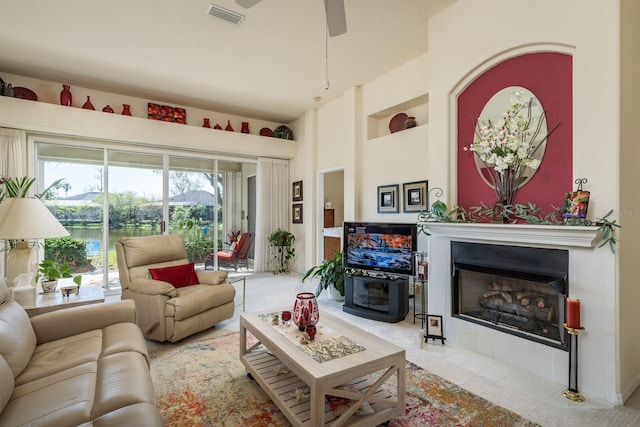 living room featuring visible vents, a fireplace, a high ceiling, and a ceiling fan