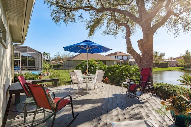 wooden deck featuring outdoor dining area, a water view, and glass enclosure