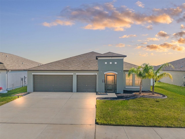 view of front of house with stucco siding, a front lawn, concrete driveway, an attached garage, and a shingled roof