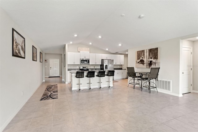 kitchen with visible vents, a breakfast bar, a kitchen island with sink, white cabinetry, and appliances with stainless steel finishes