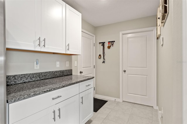 kitchen featuring light tile patterned floors, dark stone countertops, white cabinetry, and baseboards