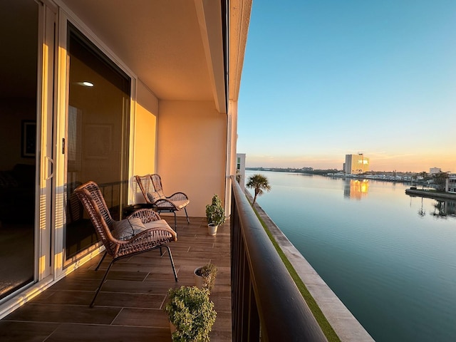 balcony at dusk featuring a water view