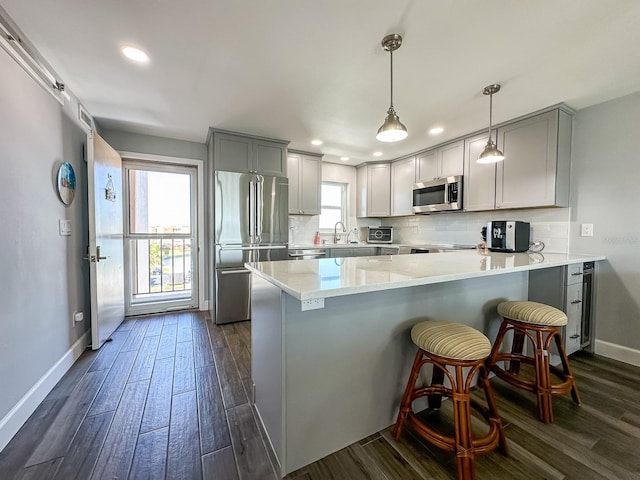 kitchen with tasteful backsplash, dark wood finished floors, gray cabinets, a peninsula, and stainless steel appliances