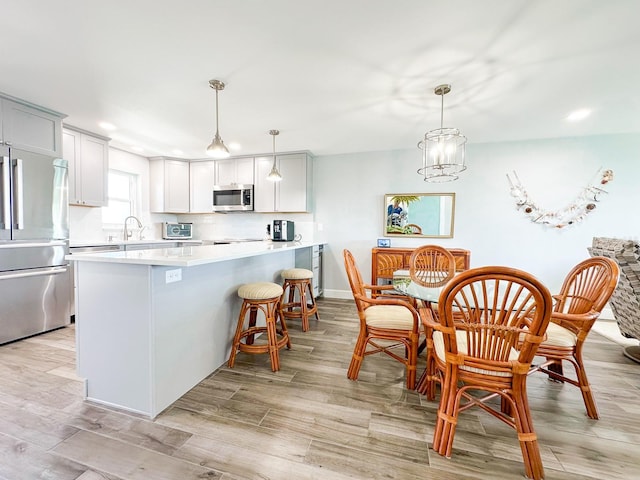 kitchen with hanging light fixtures, light countertops, appliances with stainless steel finishes, a kitchen breakfast bar, and light wood-type flooring