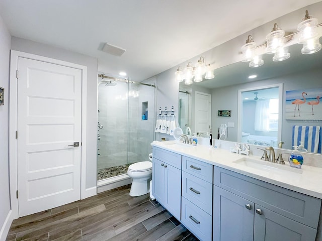 bathroom featuring toilet, a sink, wood finished floors, a shower stall, and double vanity