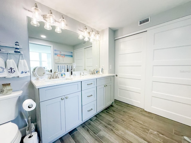 full bathroom featuring visible vents, wood tiled floor, double vanity, a sink, and toilet