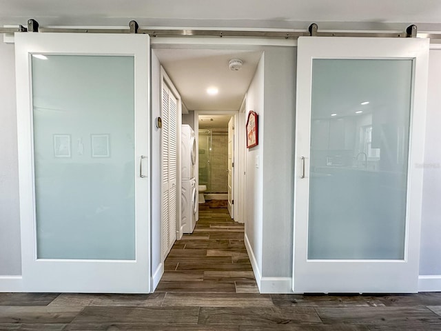 hall with dark wood finished floors, a barn door, and baseboards