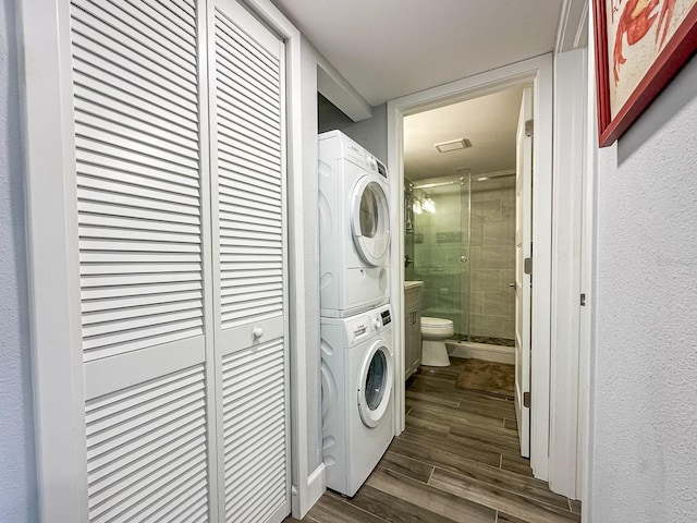 clothes washing area featuring dark wood-style floors, laundry area, and stacked washing maching and dryer