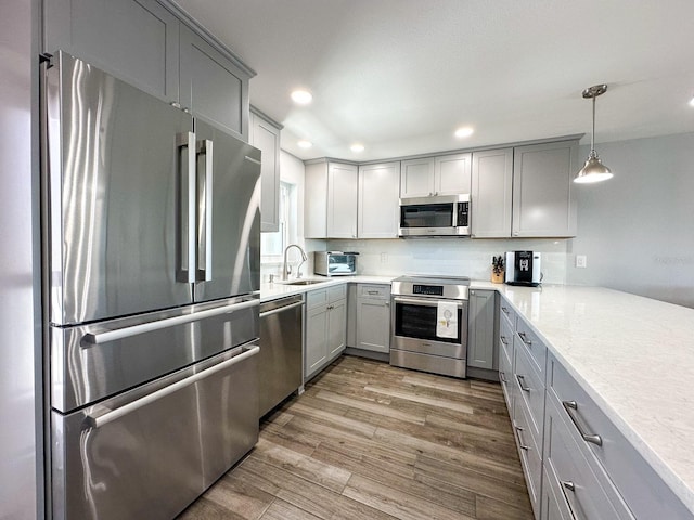 kitchen featuring a sink, decorative backsplash, gray cabinetry, appliances with stainless steel finishes, and light wood-type flooring