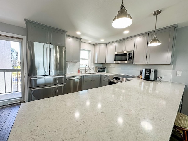 kitchen featuring light stone countertops, gray cabinets, a sink, stainless steel appliances, and tasteful backsplash