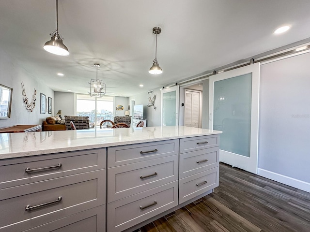 kitchen featuring pendant lighting, gray cabinets, open floor plan, light stone countertops, and dark wood-style flooring