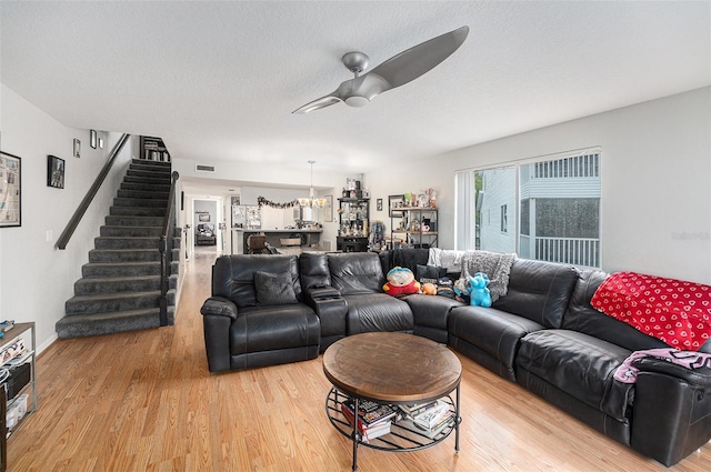 living room with light wood-type flooring, visible vents, ceiling fan with notable chandelier, a textured ceiling, and stairway