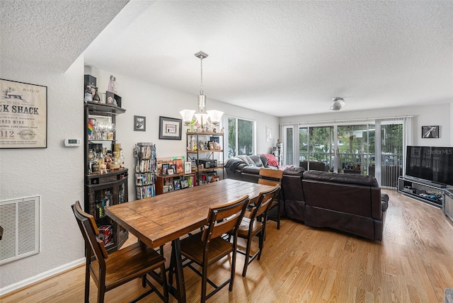 dining room featuring baseboards, visible vents, light wood-style floors, a textured ceiling, and a chandelier