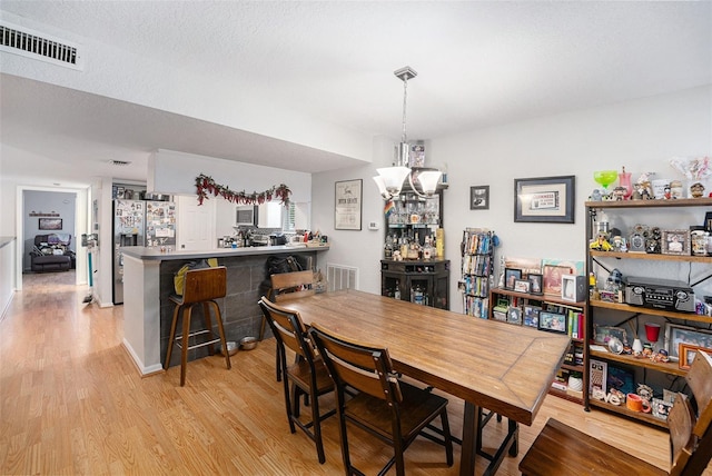 dining space with a notable chandelier, visible vents, a textured ceiling, and light wood-type flooring