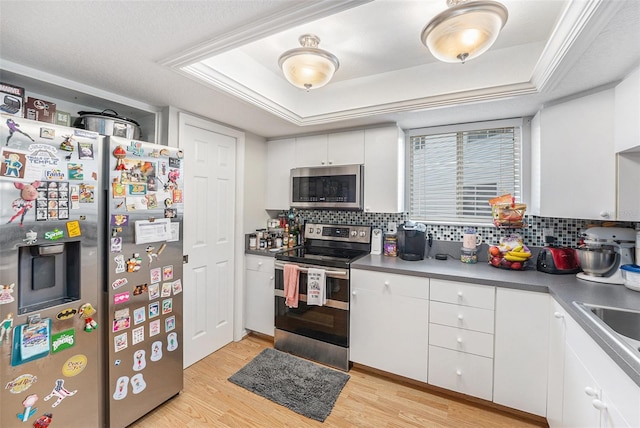 kitchen with a tray ceiling, light wood-type flooring, and stainless steel appliances