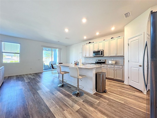 kitchen featuring a breakfast bar area, visible vents, light wood-style flooring, an island with sink, and appliances with stainless steel finishes