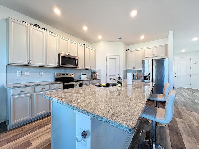 kitchen with a breakfast bar area, a sink, decorative backsplash, light wood-style floors, and appliances with stainless steel finishes