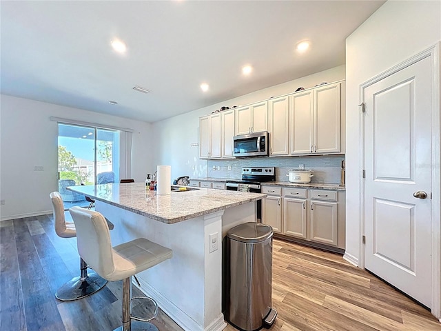 kitchen with light wood-style flooring, an island with sink, decorative backsplash, appliances with stainless steel finishes, and a kitchen bar