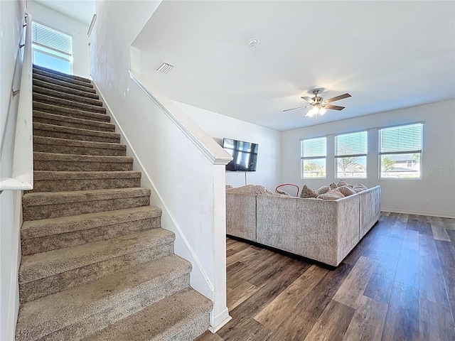 unfurnished living room featuring visible vents, a ceiling fan, dark wood finished floors, baseboards, and stairs