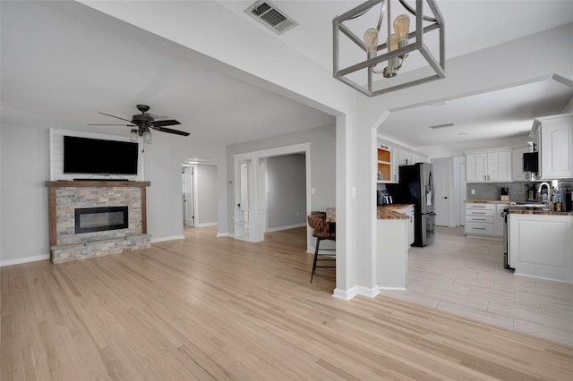 unfurnished living room featuring baseboards, arched walkways, a sink, light wood-style floors, and ceiling fan with notable chandelier