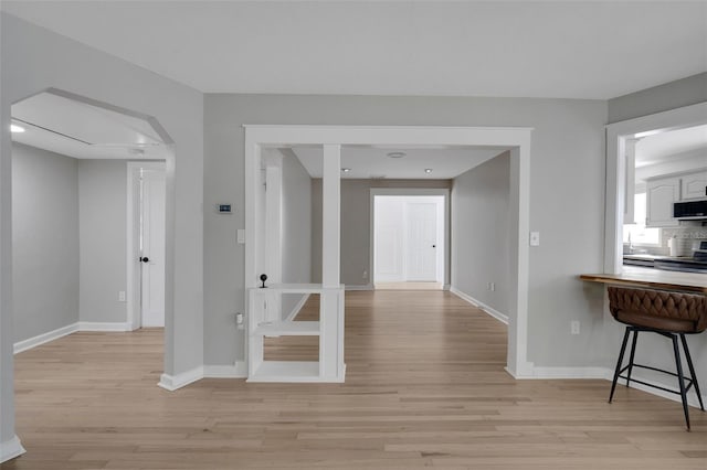 hallway featuring light wood-style flooring, arched walkways, and baseboards