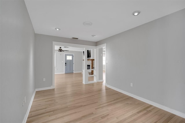 empty room with visible vents, a fireplace, light wood-type flooring, and baseboards