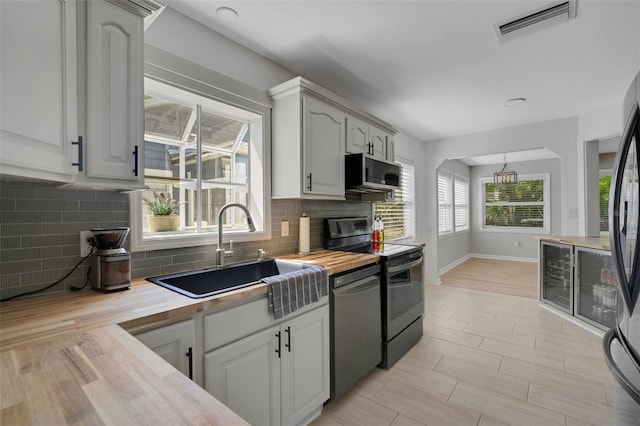 kitchen with visible vents, wooden counters, decorative backsplash, black appliances, and a sink