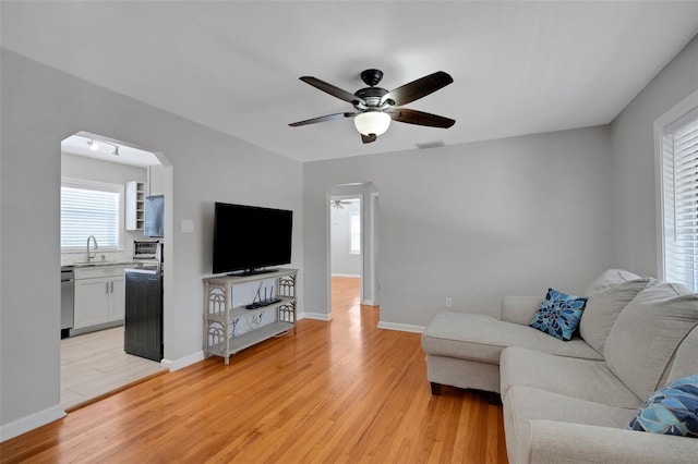 living area with light wood-style flooring, baseboards, arched walkways, and ceiling fan