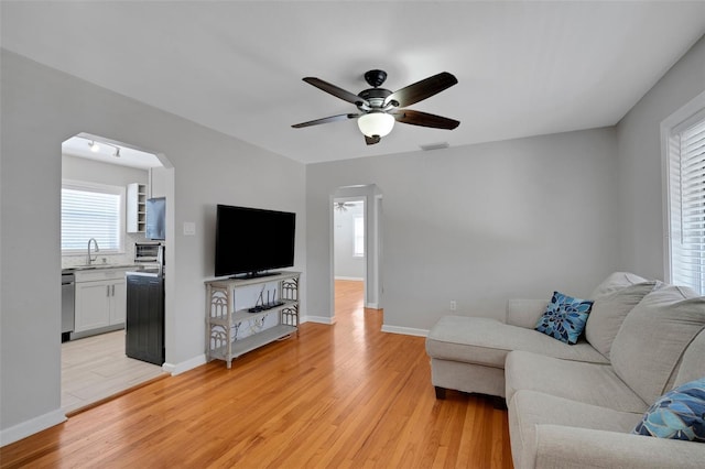 living room featuring a ceiling fan, arched walkways, light wood finished floors, and baseboards