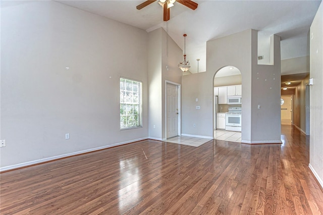 interior space featuring baseboards, arched walkways, ceiling fan, a towering ceiling, and light wood-type flooring