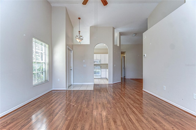 unfurnished living room with baseboards, light wood finished floors, a high ceiling, arched walkways, and ceiling fan