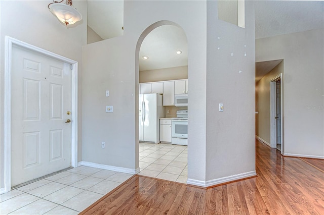 entryway featuring arched walkways, light tile patterned floors, and baseboards