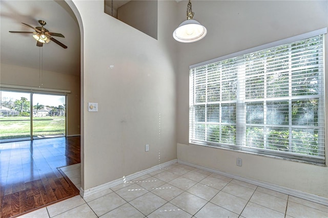 empty room featuring a wealth of natural light, arched walkways, a ceiling fan, and light tile patterned floors