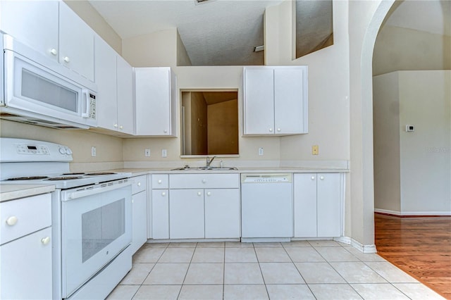 kitchen featuring white appliances, light tile patterned floors, arched walkways, a sink, and light countertops