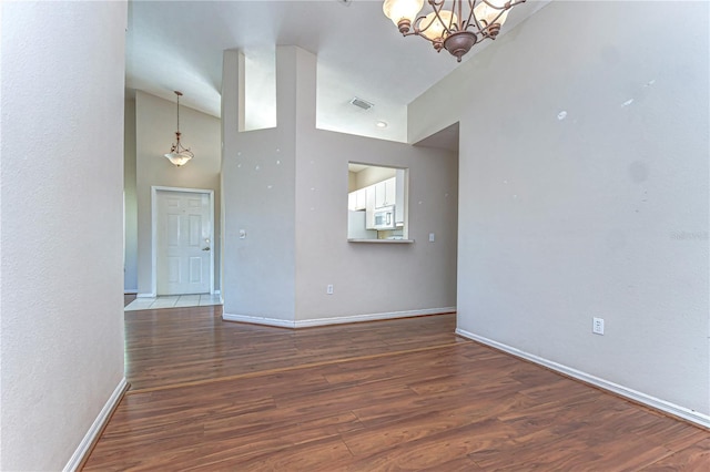 spare room featuring visible vents, a notable chandelier, high vaulted ceiling, wood finished floors, and baseboards