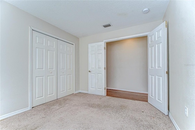 unfurnished bedroom with visible vents, a textured ceiling, a closet, carpet flooring, and baseboards