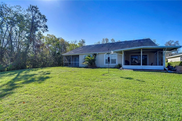 rear view of house featuring stucco siding, a lawn, and a sunroom